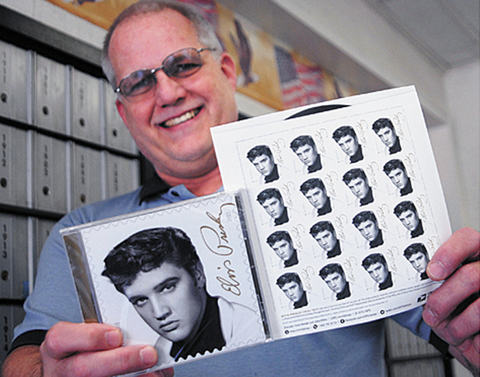 Employee shows a sheet of Music Icons: Elvis Presley stamps, along with the “Elvis Presley Forever” CD