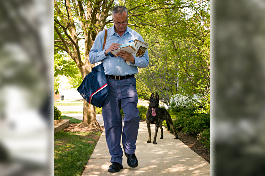 A letter carrier being followed by a dog.