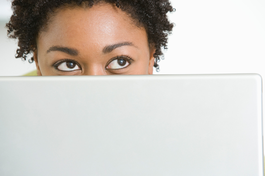 A woman peaking out from behind a laptop computer.