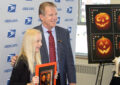 Chief Financial Officer Joe Corbett (right) and St. Stephen’s Catholic School student Samantha Jenson (left) pose for a picture with a pane of Jack-o’-lantern stamps.
