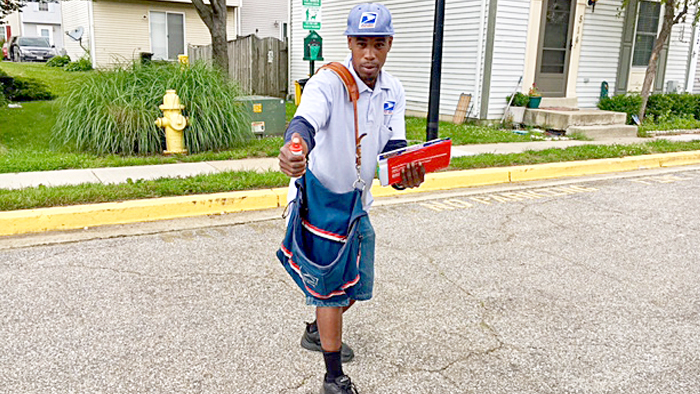 Male letter carrier holds mail and dog spray