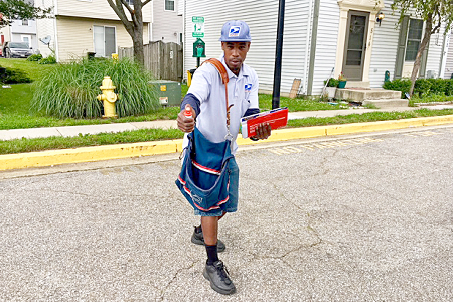 Male letter carrier holds mail and dog spray