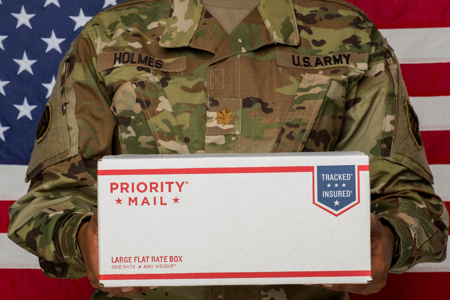 Person wearing Army uniform holding Priority Mail box