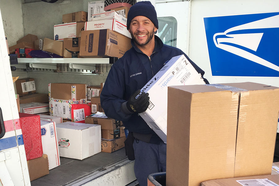 Letter carrier holds package near delivery vehicle