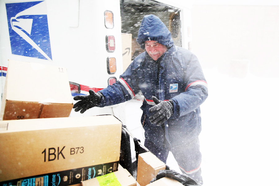 Postal worker loads vehicle as wind blows heavy snow