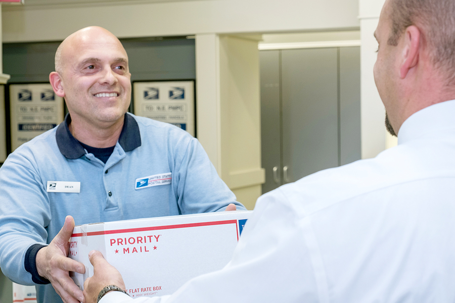 Postal employee hands man package at retail counter