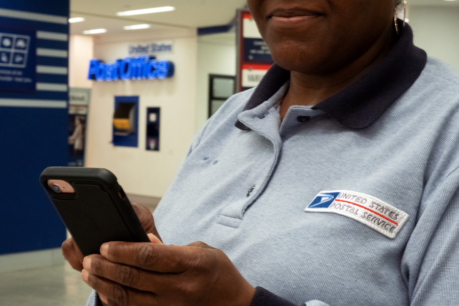 Uniformed postal worker uses cell phone inside Post Office lobby