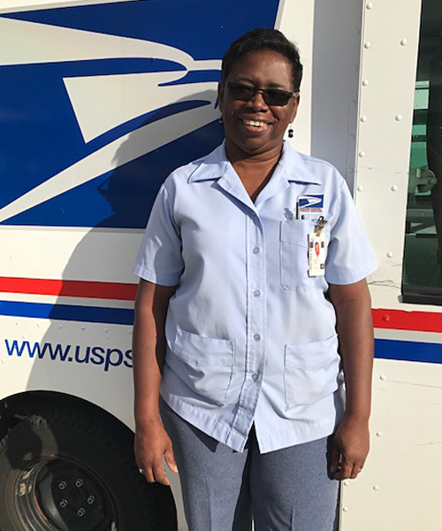 Smiling woman in postal uniform stands next to delivery vehicle