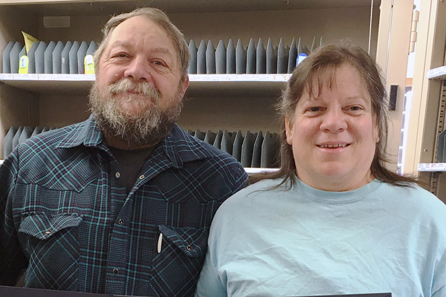 Smiling man, woman stand inside Post Office work room