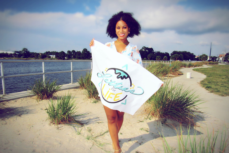 Woman stands on beach, holding flag with Letters for Life logo