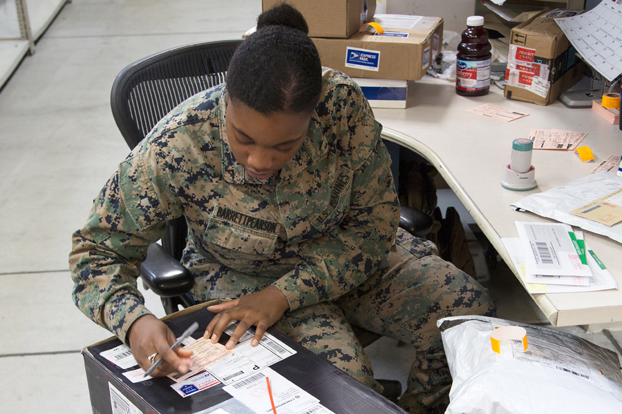 Marine sits at desk, completing postal paperwork