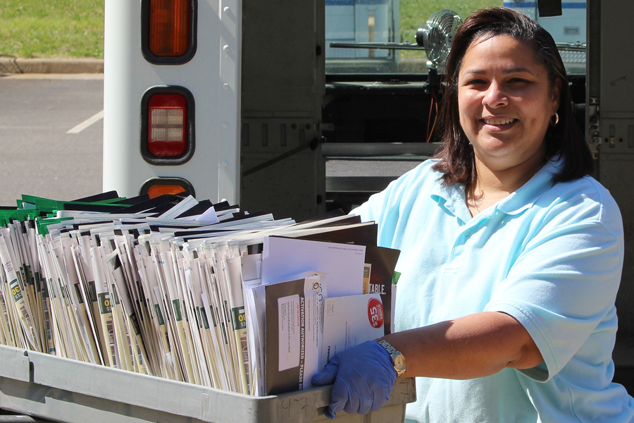 Postal worker holds mail tray near delivery vehicle