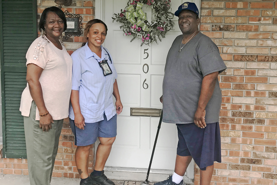 Smiling postal worker stands on front stoop with man, woman