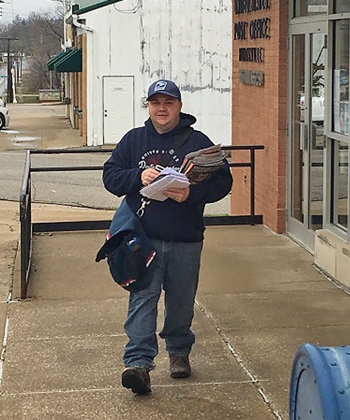 Postal worker walks down street, holding mail