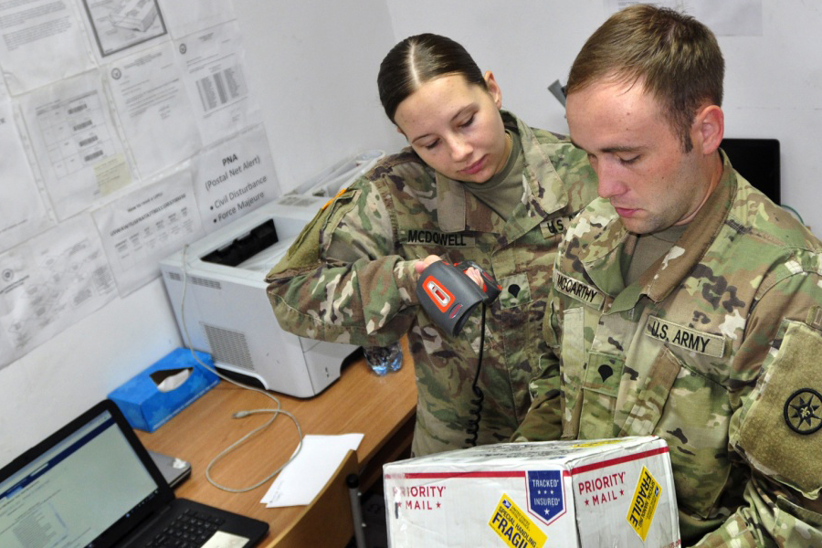 Army soldier scans package with handheld device as another soldier watches