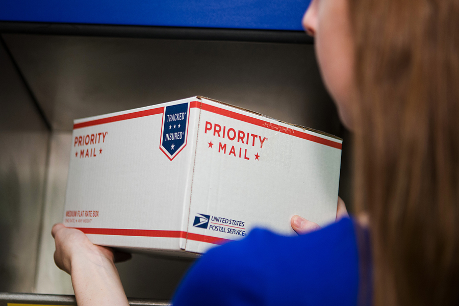 Woman puts Priority Mail package in Post Office receptacle
