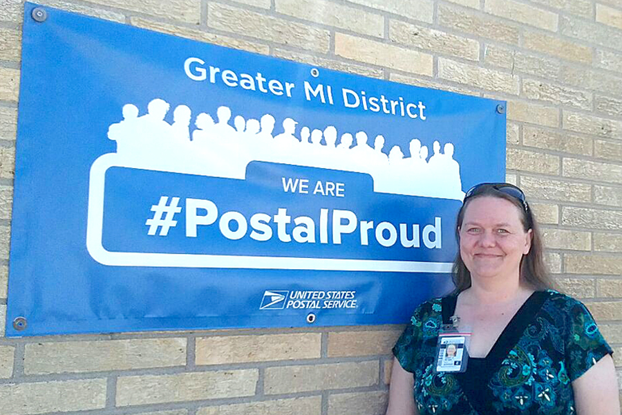 Retail Assoicate stands proudly in front of #PostalProud sign