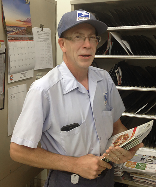 Smiling letter carrier stands in postal workroom