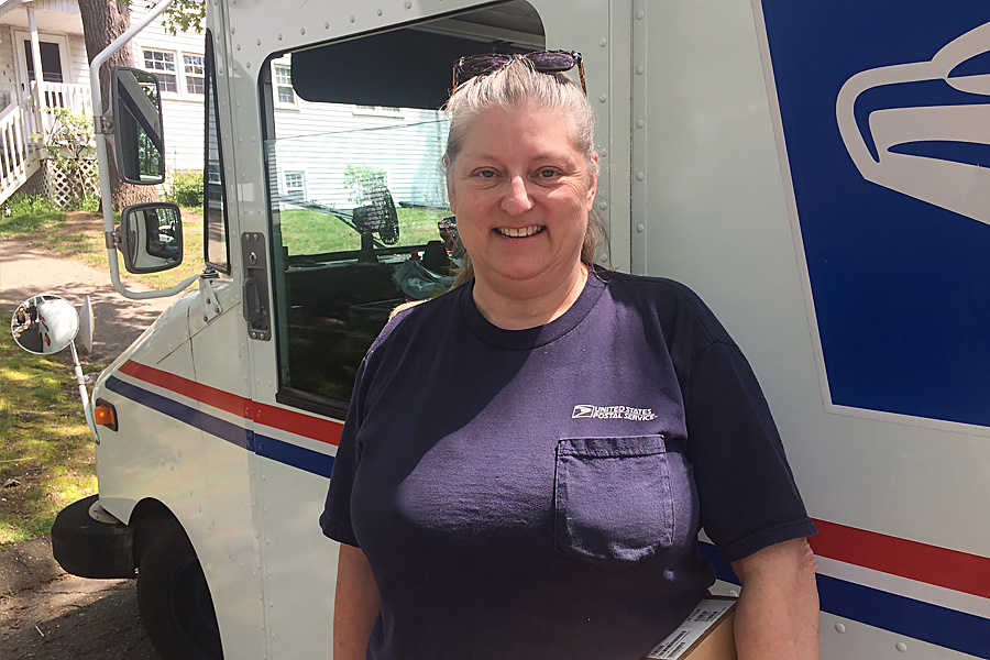Smiling woman stands next to postal delivery vehicle