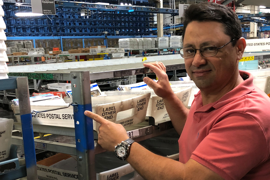 Smiling postal worker stands near equipment inside plant