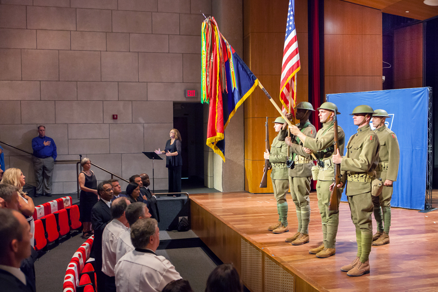 Soldiers dressed in World War I-era uniforms hold flags in front of audience