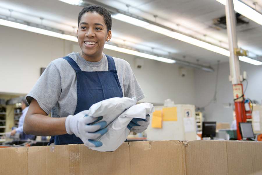 Smiling woman holds package inside Post Office workroom