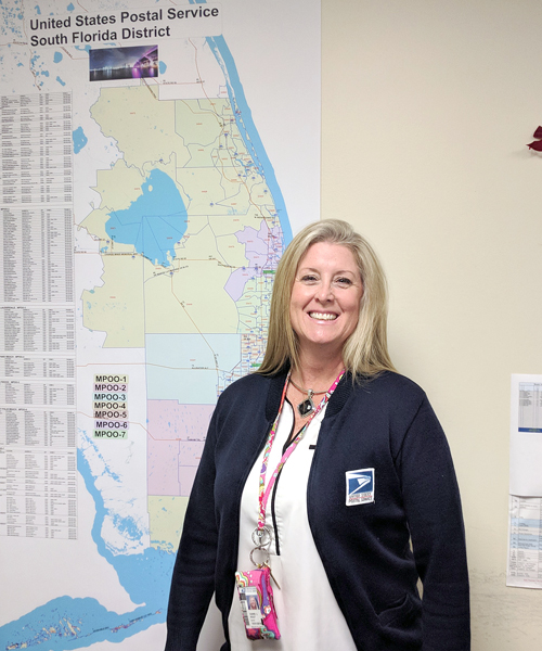 Smiling postal worker stands next to map on wall
