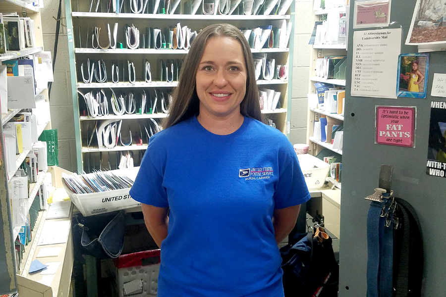Smiling woman stands in postal workroom