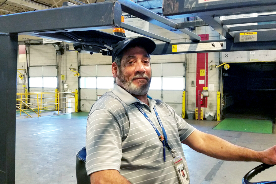 Man sits behind wheel of forklift inside postal plant
