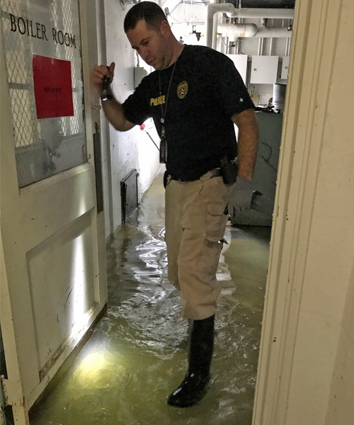 Man wearing police gear wades through flooded basement
