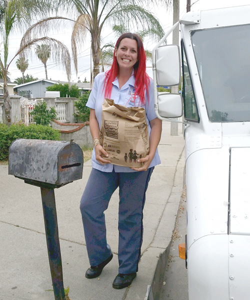 Smiling letter carrier holds grocery bag full of food