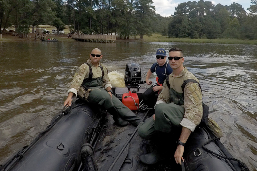 Three men wearing military uniforms travel in boat through murky waters