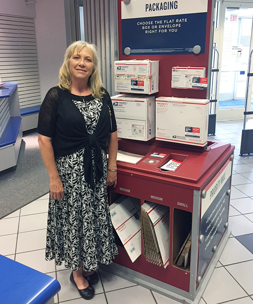 Woman stands next to Priority Mail display in Post Office