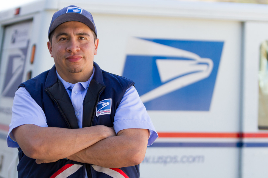 Smiling letter carrier stands near delivery vehicle