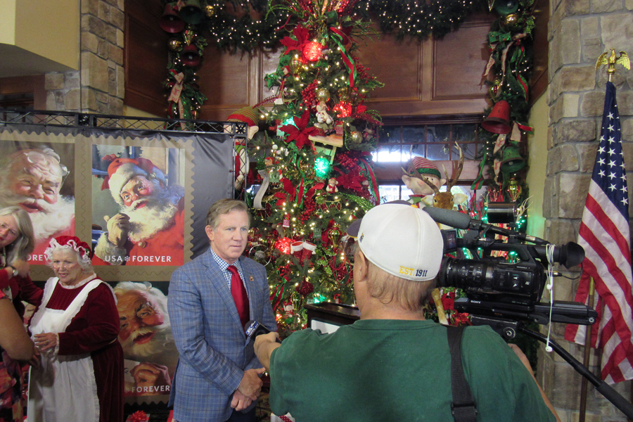 Man wearing suit is interviewed by TV news crew near Christmas tree