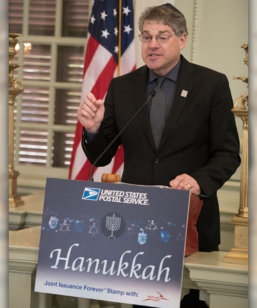 Man gestures at podium decorated with Hanukkah stamp image