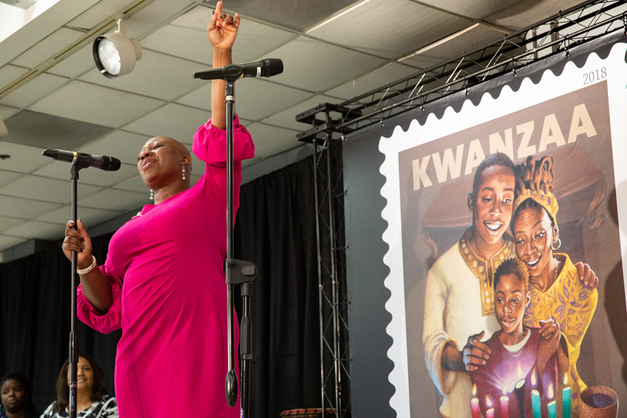 African-American woman strikes dramatic pose on stage near Kwanzaa stamp artwork