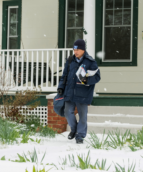 Letter carrier walks on sidewalk in snowy neighborhood