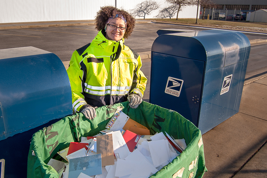 Postal worker stands next to bin full of mail