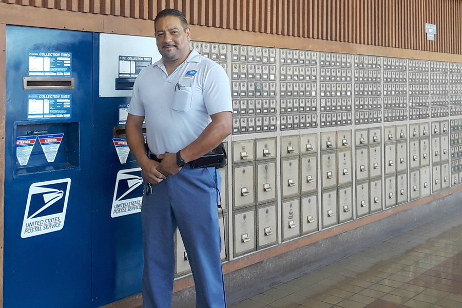 Smiling postal worker stands next to bank of PO Boxes