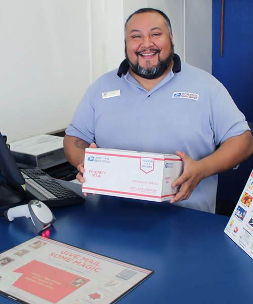 Smiling postal worker holds package at Post Office retail counter