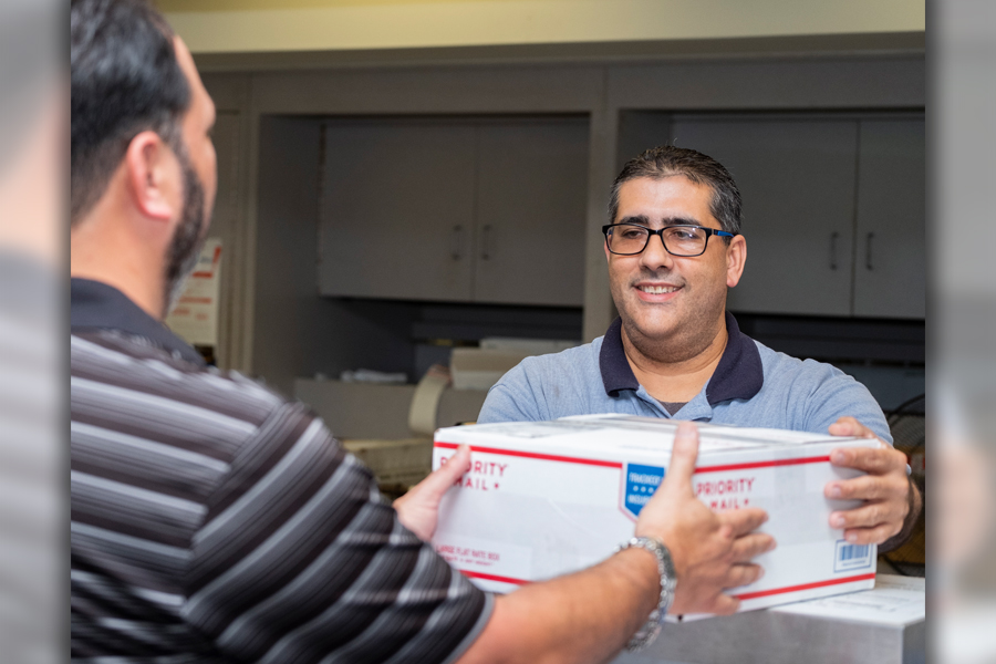 Customer hands package to smiling postal worker at Post Office counter