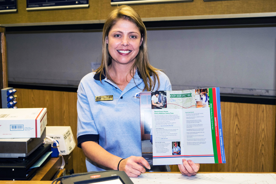 Smiling postal retail worker stands at counter holding brochure