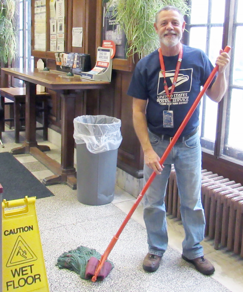 Smiling custodian holds mop and bucket in Post Office lobby