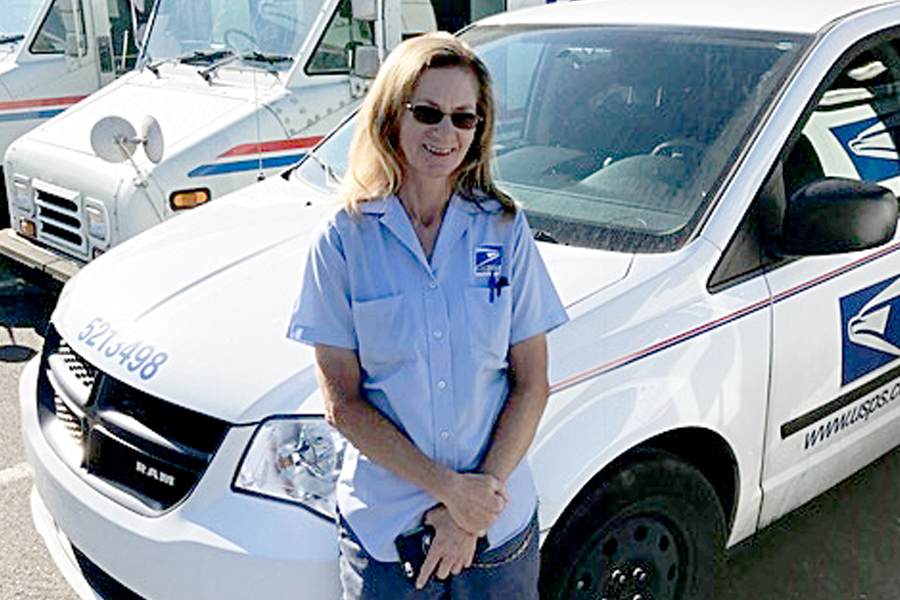 USPS letter carrier stands next to delivery vehicle