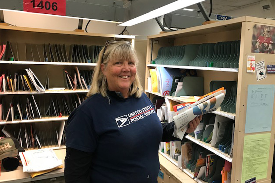 Smiling woman sorts mail in postal workroom