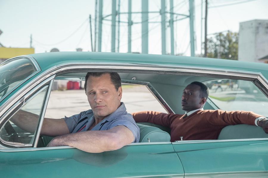 Publicity still showing actor driving 1960s car with other actor in backseat
