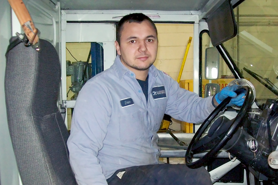 Man in postal uniform sits inside delivery vehicle