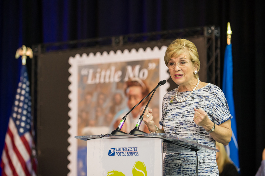 Woman stands at podium near Little Mo stamp poster