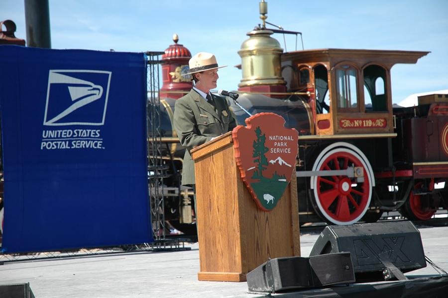 Park ranger speaks at podium in front of historic trains